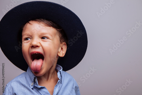 a funny kid in a hat shows his tongue and laughs. in the studio, on a white background, a large portrait horizontal.