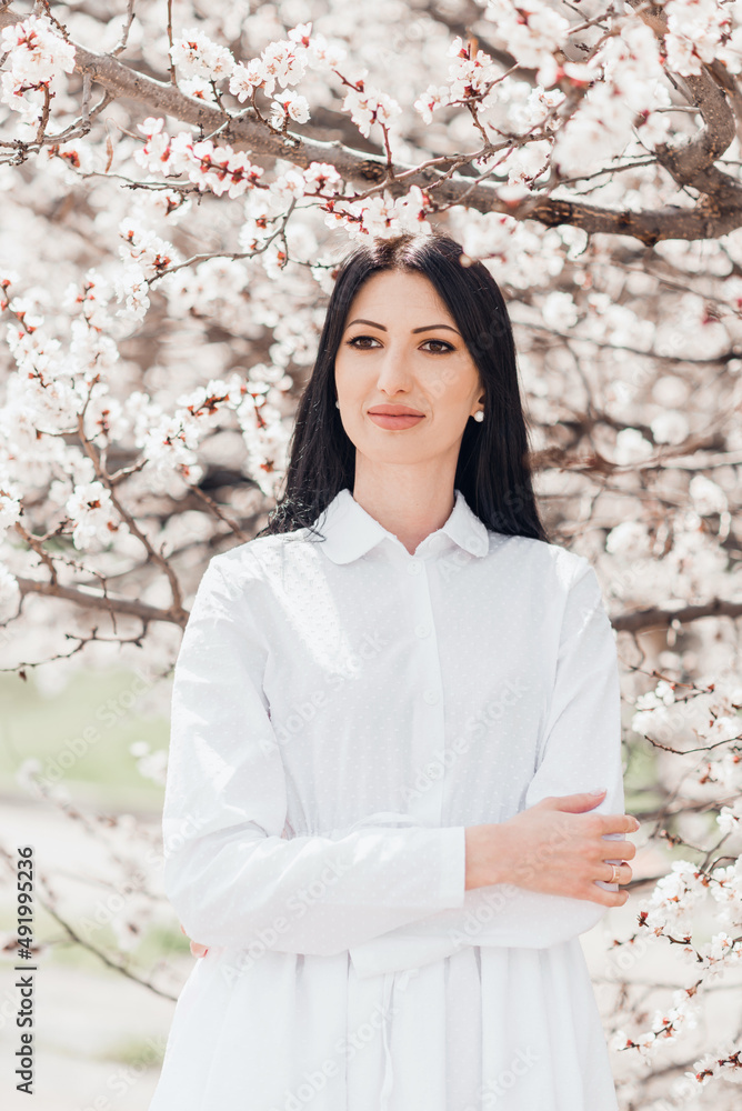 Portrait of pretty brunette girl posing against the spring blooming trees in the garden.