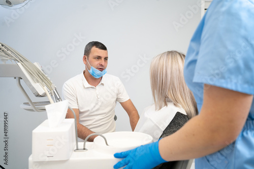 beautiful caucasian girl with a toothache sits in a dental chair. A professional male dentist helps his female patient in pain. painful help in treatment.