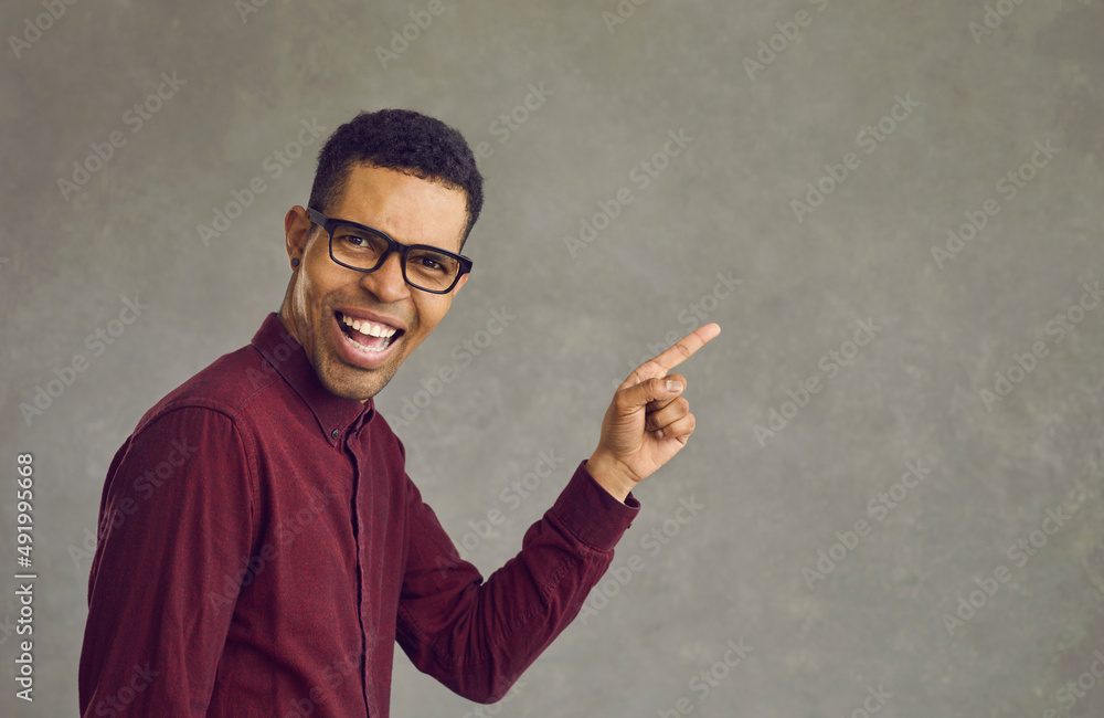 Handsome young african american man in eyeglasses laughing looking at camera pointing finger on studio copy space presenting something. People positive emotion for advertisement concept Handsome young african american man in eyeglasses laughing looking at camera pointing finger on studio copy space presenting something. People positive emotion for advertisement concept