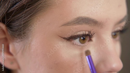A young beautiful girl does makeup in the studio paints eyelashes, eyebrows, lips looks in the mirror close-up. Makeup of a girl's face close-up in the studio in front of a mirror.