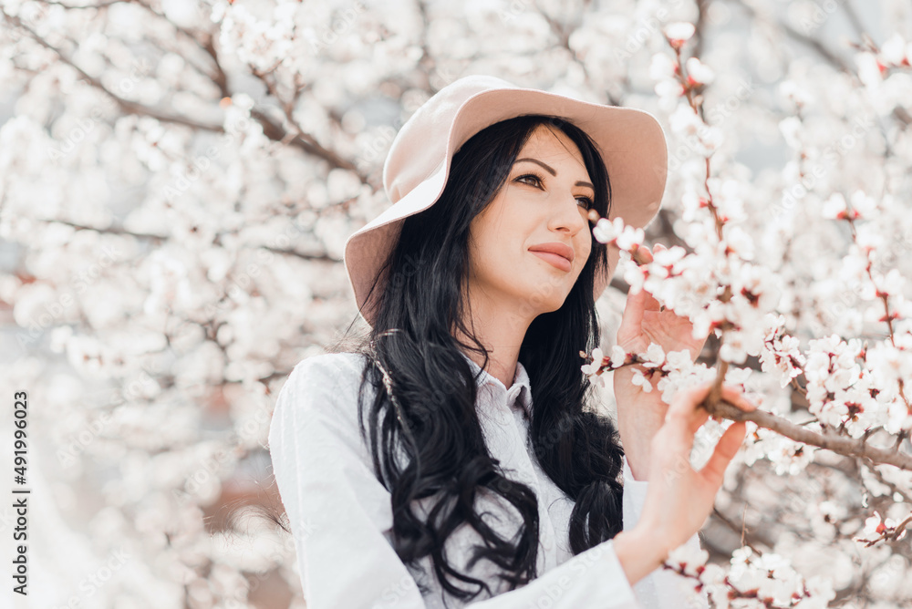Portrait of pretty brunette girl posing against the spring blooming trees in hat. Portrait of pretty brunette girl posing against the spring blooming trees in hat.