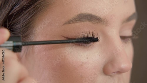 A young beautiful girl does makeup in the studio paints eyelashes, eyebrows, lips looks in the mirror close-up. Makeup of a girl's face close-up in the studio in front of a mirror.