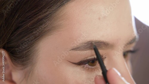 A young beautiful girl does makeup in the studio paints eyelashes, eyebrows, lips looks in the mirror close-up. Makeup of a girl's face close-up in the studio in front of a mirror.