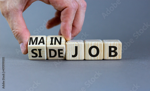 Extra or side job symbol. Businessman turns wooden cubes and changes concept words Side job to Main job. Beautiful grey table grey background, copy space. Business side or main job concept.