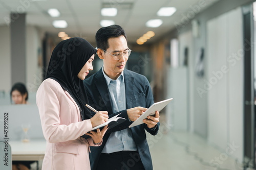 Middle-aged businessman and female secretary wearing hijab stand together in the hallway in hand using a tablet to make presentations