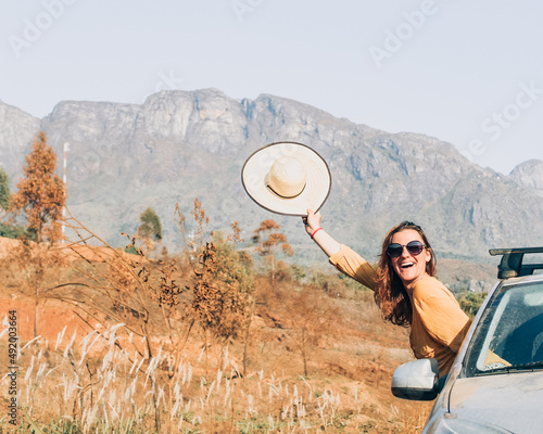 mulher com corpo para fora do carro e chapéu na mão com montanhas ao fundo  photo