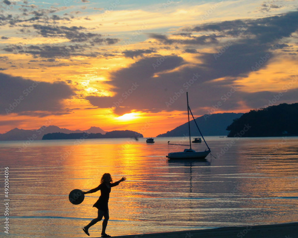 silhueta de mulher não identificada caminhando em frente ao mar em nascer do sol na praia em Paraty