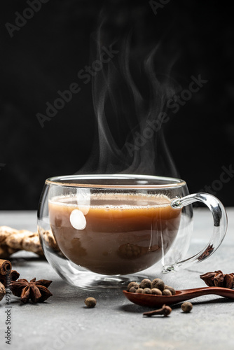 Indian masala chai tea. Hot masala chai spiced tea with milk and spices is poured into a glass glass on dark background. vertical image. place for text