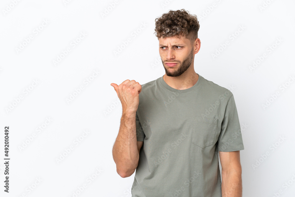 Young caucasian handsome man isolated on white background unhappy and pointing to the side Young caucasian handsome man isolated on white background unhappy and pointing to the side