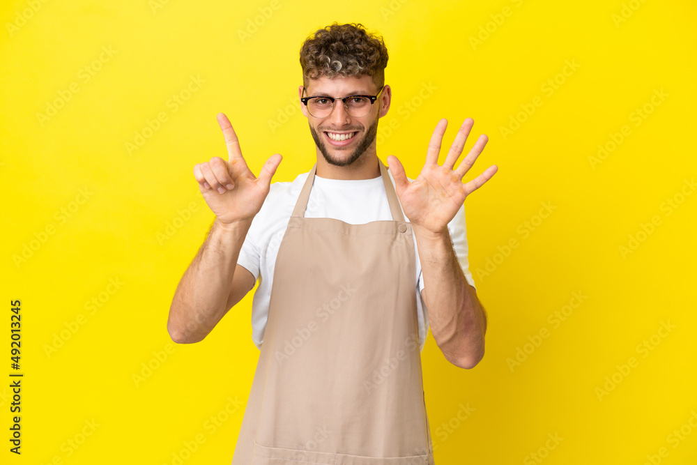 Restaurant waiter blonde man isolated on yellow background counting seven with fingers Restaurant waiter blonde man isolated on yellow background counting seven with fingers