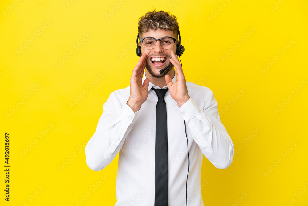 Telemarketer blonde man working with a headset isolated on yellow background shouting and announcing something Telemarketer blonde man working with a headset isolated on yellow background shouting and announcing something
