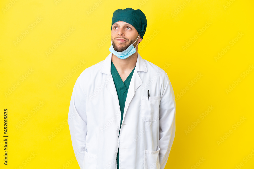 Surgeon blonde man in green uniform isolated on yellow background and looking up Surgeon blonde man in green uniform isolated on yellow background and looking up