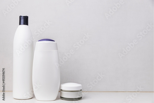 Preparation for hotel spa treatment or home bath procedure. Gray bathroom shelf or table with accessories and cosmetics. Shampoo, shower gel, hair conditioner, soft cream glass bottle with copy space