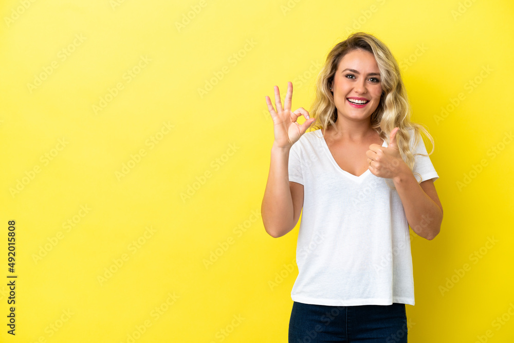 Young Brazilian woman isolated on yellow background showing ok sign and thumb up gesture Young Brazilian woman isolated on yellow background showing ok sign and thumb up gesture