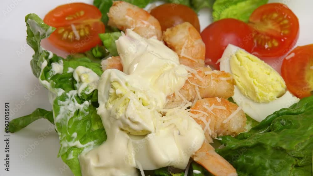 Caesar salad with shrimp. Grated cheese falls into shrimp caesar salad. Fresh vegetable salad with shrimp and seafood. Healthy food and diet nutrition. Cook preparing salad with sauce. Caesar salad with shrimp. Grated cheese falls into shrimp caesar salad. Fresh vegetable salad with shrimp and seafood. Healthy food and diet nutrition. Cook preparing salad with sauce.