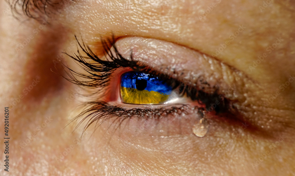Young girl crying and praying for the peace and end of war. Political conflict with the Ukrainian flag inside her iris. Tears and sadness concept for believing and having faith. Young girl crying and praying for the peace and end of war. Political conflict with the Ukrainian flag inside her iris. Tears and sadness concept for believing and having faith.