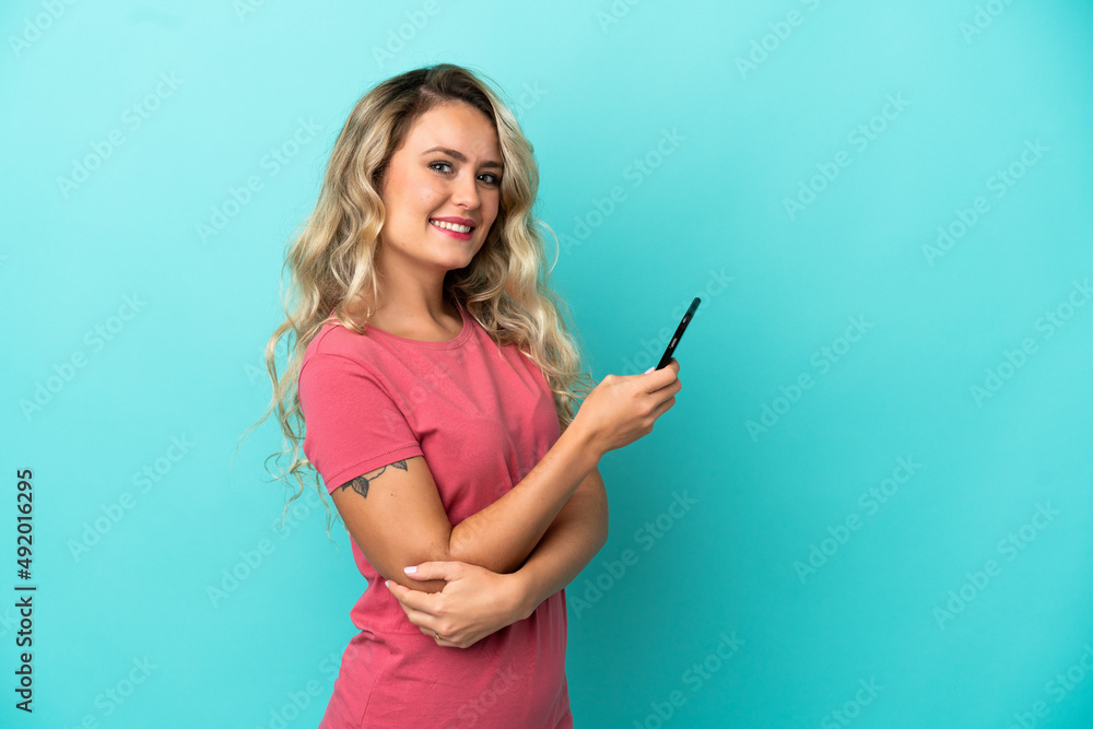 Young Brazilian woman isolated on blue background holding a mobile phone and with arms crossed Young Brazilian woman isolated on blue background holding a mobile phone and with arms crossed