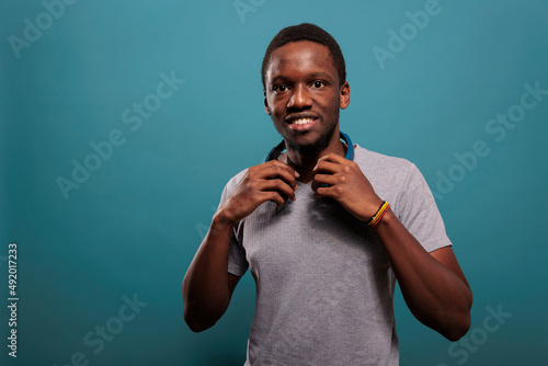 Portrait of african american guy having wireless headphones to listen to mp3 music for leisure in studio. Millennial person using headset audio technology and smiling in front of camera.