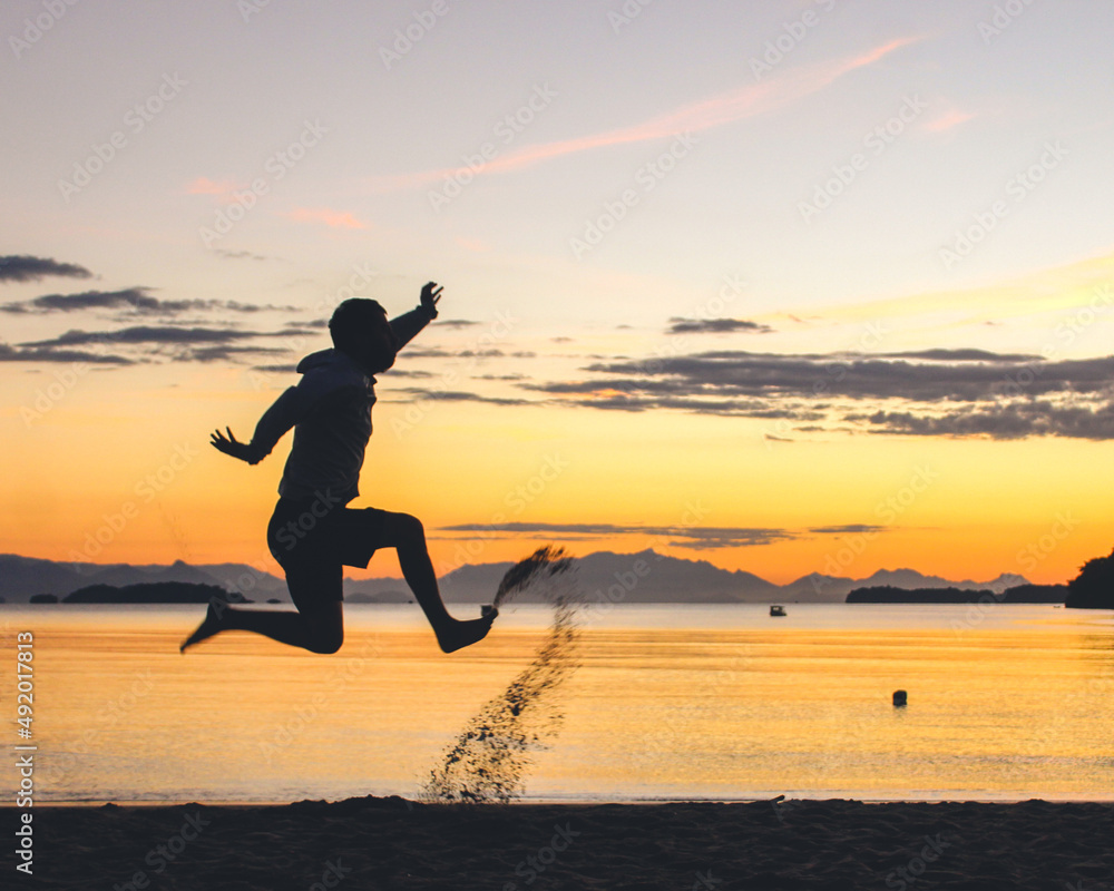 silhueta de homem não identificado pulando na praia durante o nascer do sol 