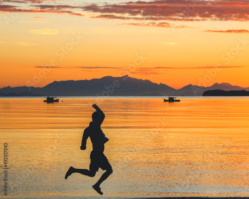 silhueta de homem n  o identificado pulando na praia durante o nascer do sol 