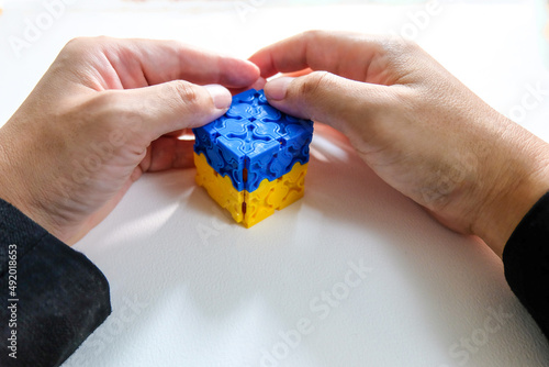 Two hands covering blue and yellow cube on white background