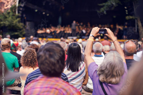 Small cameras capture great memories. Shot of a person in the crowd holding a camera to photograph a classical concert.
