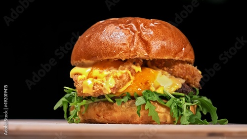 Craft burger is cooking on black background in black food gloves. Consist: sauce, arugula, tomato, red onion rings fries, cucumber, cheese, air bun and marble meat beef. Not made ideal. Looks real