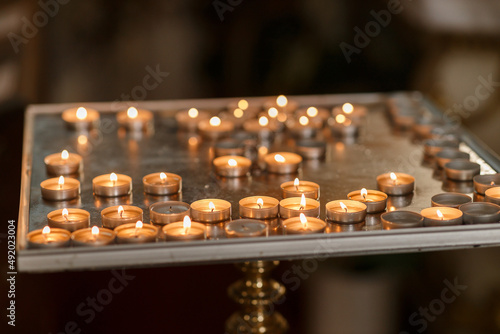 many small burning candles in the church on a stand