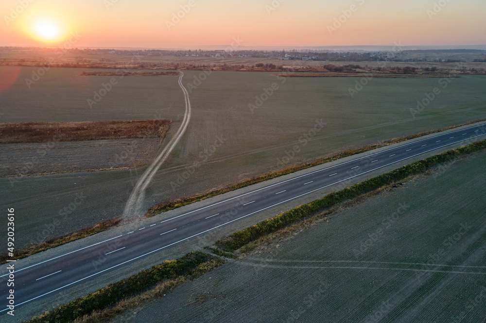 Fototapeta premium Aerial view of empty intercity road with asphalt surface and white markings in evening