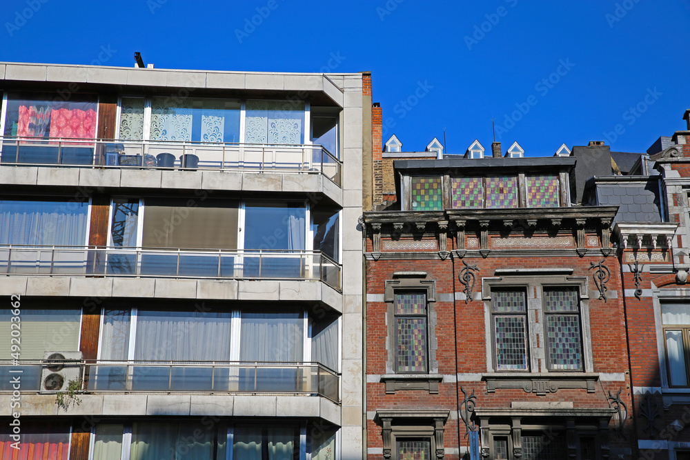 View on two facades side by side together with blue sky. Modern appartment building is neglected and in need of renovation, old medieval brick house in good condition - Liege, Belgium (focus on center
