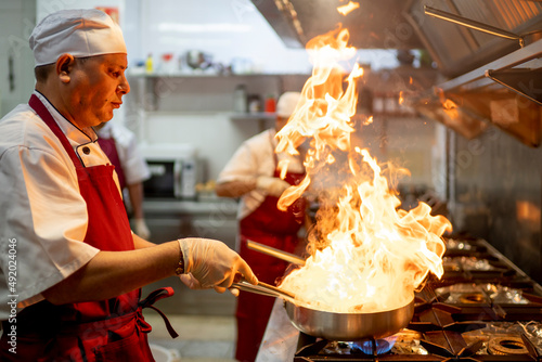 Fotografie Indian chef cooking in industrial kitchen with the burning pan