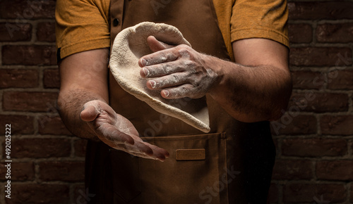 flying pizza dough with flour scattering in a freeze motion of a cloud of flour midair on black. Cook hands kneading dough. copy space