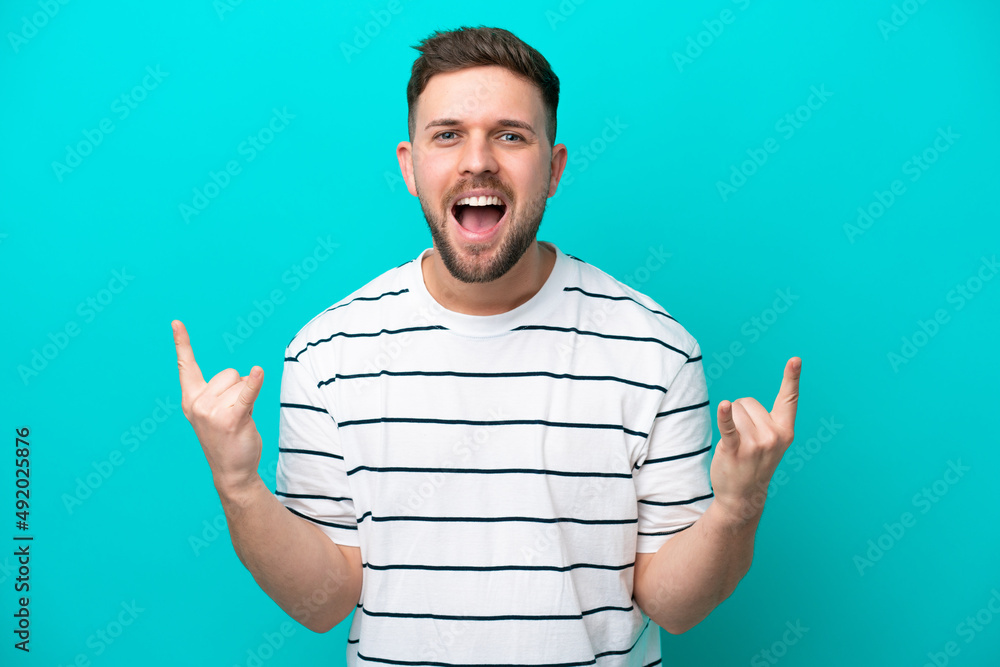 Young caucasian man isolated on blue background making horn gesture Young caucasian man isolated on blue background making horn gesture