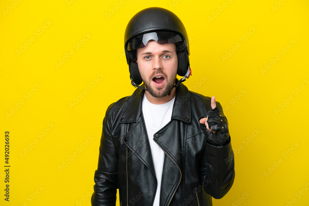 Young caucasian man with a motorcycle helmet isolated on yellow background intending to realizes the solution while lifting a finger up Young caucasian man with a motorcycle helmet isolated on yellow background intending to realizes the solution while lifting a finger up