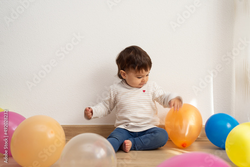 Little girl sitting on floor and playing with balloons of different colors. 
