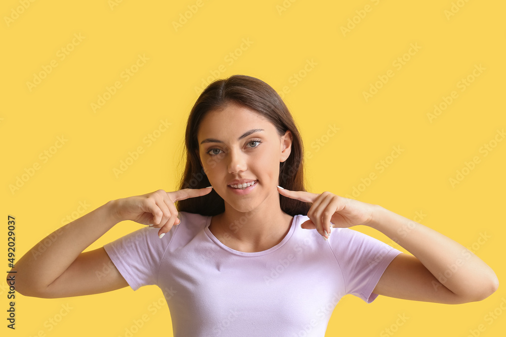 Pretty teenage girl pointing at dental braces on yellow background Pretty teenage girl pointing at dental braces on yellow background