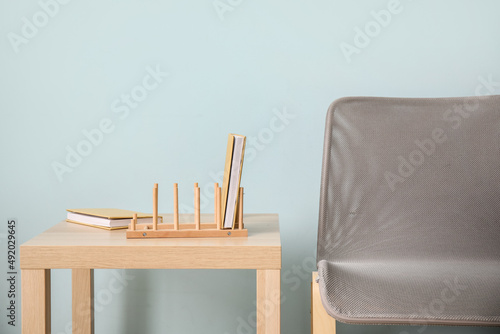 Wooden organizer with books on table and chair near blue wall