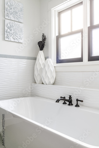 Contemporary Freestanding Bathtub. White bathroom with white custom tile and black faucet. Modern decor with windows. photo