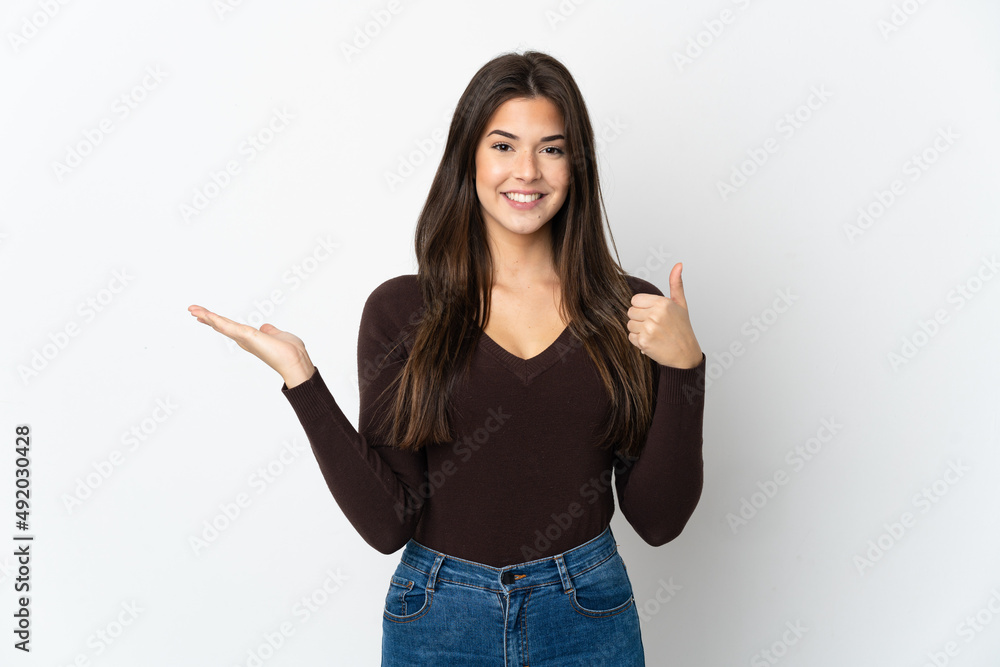 Teenager Brazilian girl isolated on white background holding copyspace imaginary on the palm to insert an ad and with thumbs up Teenager Brazilian girl isolated on white background holding copyspace imaginary on the palm to insert an ad and with thumbs up