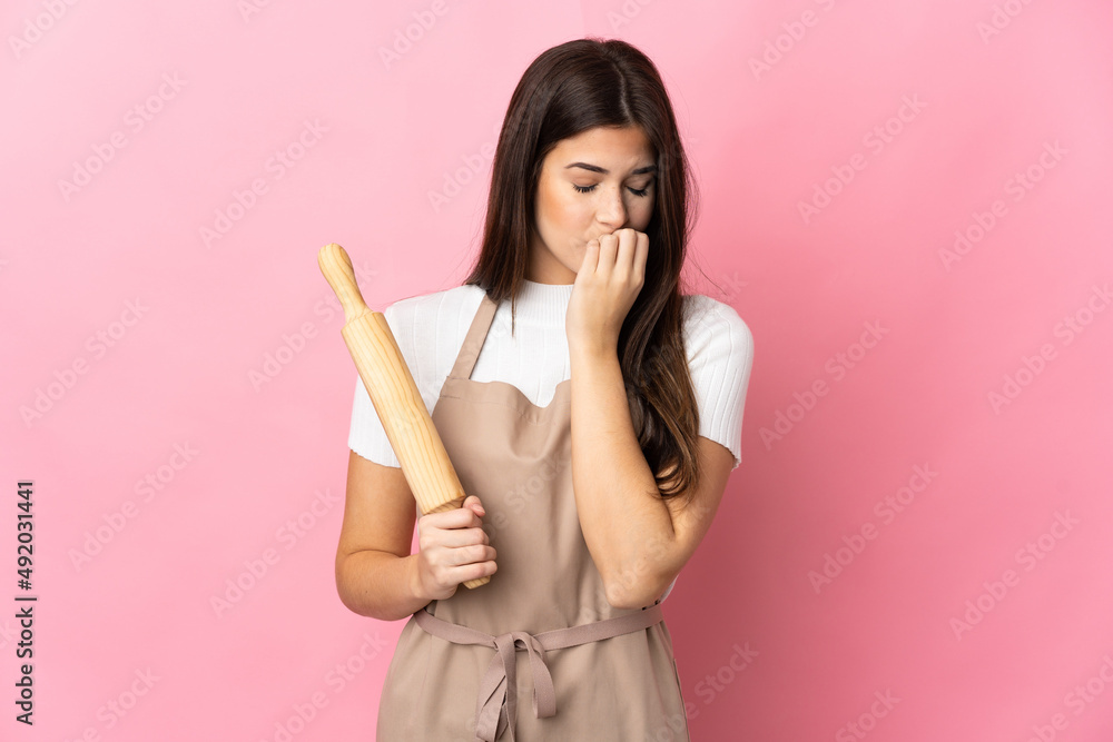 Teenager Brazilian girl holding a rolling pin isolated on pink background having doubts Teenager Brazilian girl holding a rolling pin isolated on pink background having doubts