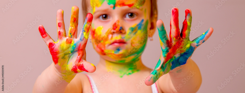 Humorous image of childrens makeup. Beauty, fashion, happy childhood concept. Close up portrait of beautiful young child girl with painted face and hands. Selective focus on hands.