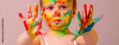 Humorous image of childrens makeup. Beauty, fashion, happy childhood concept. Close up portrait of beautiful young child girl with painted face and hands. Selective focus on hands.