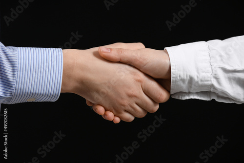 Business partners shaking hands on black background, closeup