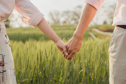 couple holding hands in a green field at sunset