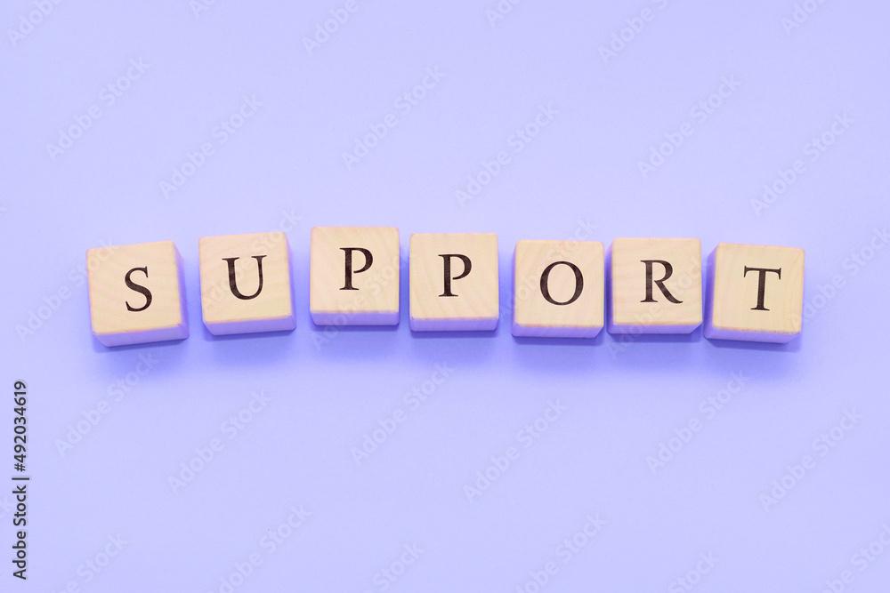 The word SUPPORT is made of wooden cubes on a violet background. The word SUPPORT is made of wooden cubes on a violet background.