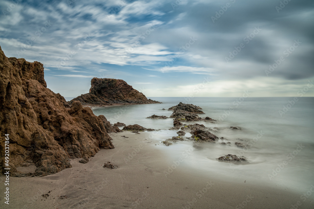 long exposure of a picturesque small beach in a rocky cove with reef at low tide