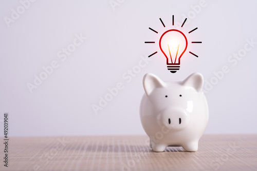 saving energy economy and money concept. creative idea for save or investment. piggy bank on desk with light bulb icon planning money finance. Copy space for text.