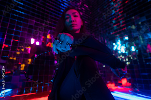 Asian man holding sunglasses. Neon photo studio. 