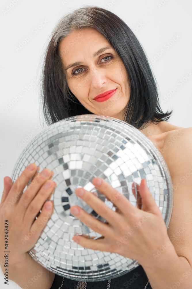 Studio photo of middle aged woman starting getting grey-haired wearing black clothes with silver disco ball in hands on white background, middle age sexy lady, happy life concept Studio photo of middle aged woman starting getting grey-haired wearing black clothes with silver disco ball in hands on white background, middle age sexy lady, happy life concept